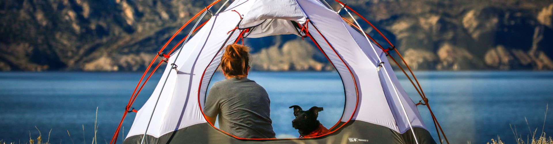 Zelt mit Seeblick, Frau und Hund – ein selbst geplanter Moment, der nicht in Pauschalpaketen steckt.