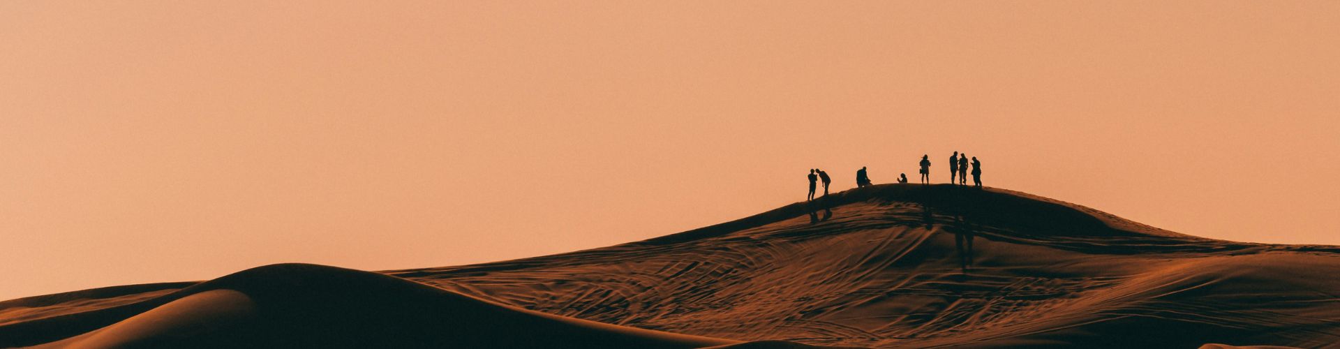 Westmongolei Silhouetten einer kleinen Reisegruppe bei Sonnenuntergang auf einer Sanddüne in Marokko. Sinnbild für eine Wüstentour ab Marrakesch.