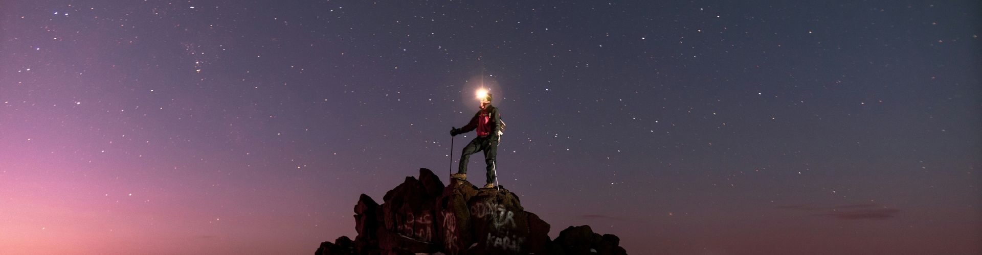 Marokko Wüstentour – Kamel in der Sahara bei Sonnenuntergang Toubkal Besteigung -Mann auf Bergspitze vor nächtlichem Himmel