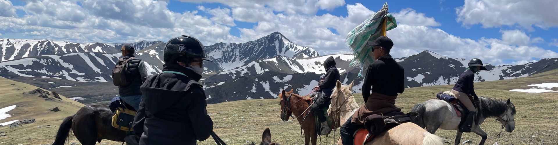 Morgennebel Reitergruppe beim Pferdetrekking durch das mongolische Altai-Gebirge vor schneebedeckten Bergen und weitem Himmel.