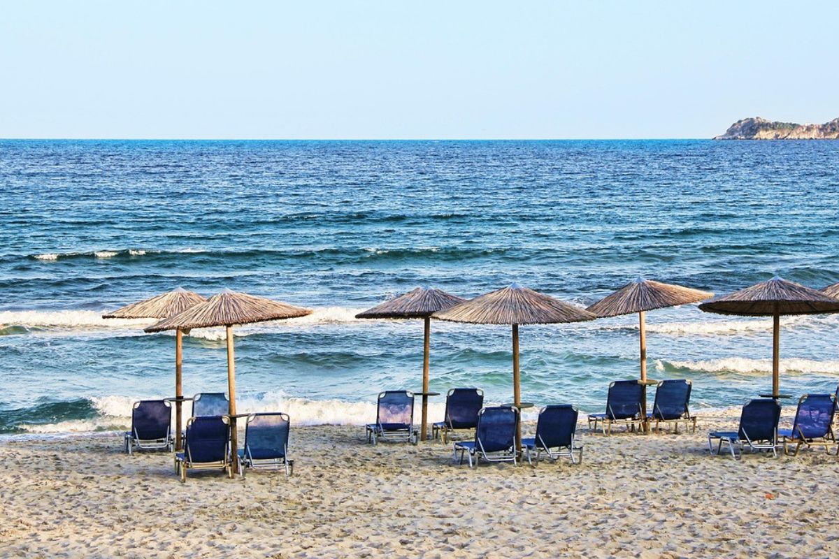Komfortzone inklusive: reservierte Liegen, Buffetzeiten und kein Platz für Überraschungen. Leere Liegestühle unter Strohsonnenschirmen an einem gepflegten Strand.