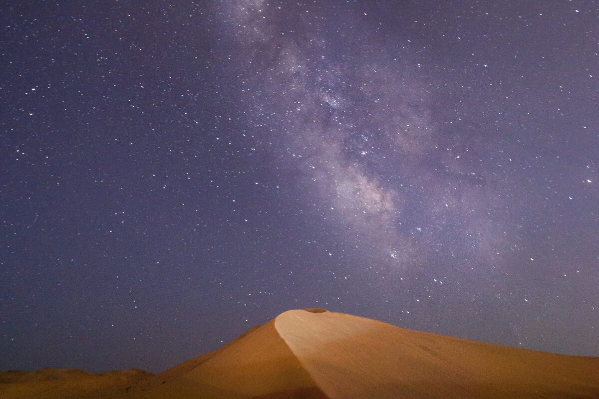 Kein Licht, kein Lärm – nur du, der Sand und ein Himmel voller Möglichkeiten. Klarer Sternenhimmel mit Milchstraße über einer Sanddüne in der Wüste.
