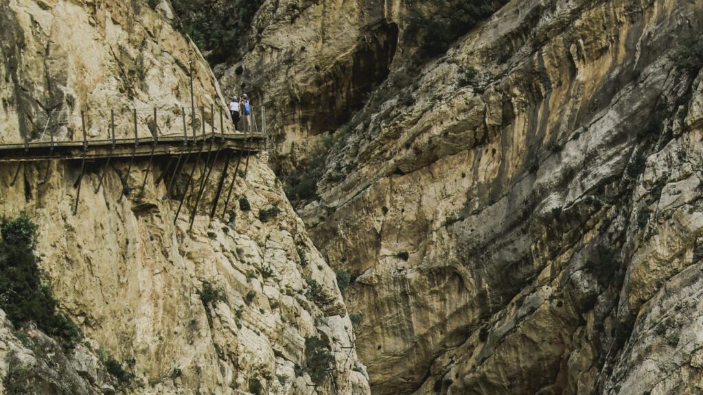 Wanderer auf schmalem Steg des Caminito del Rey an steiler Felswand in Andalusien