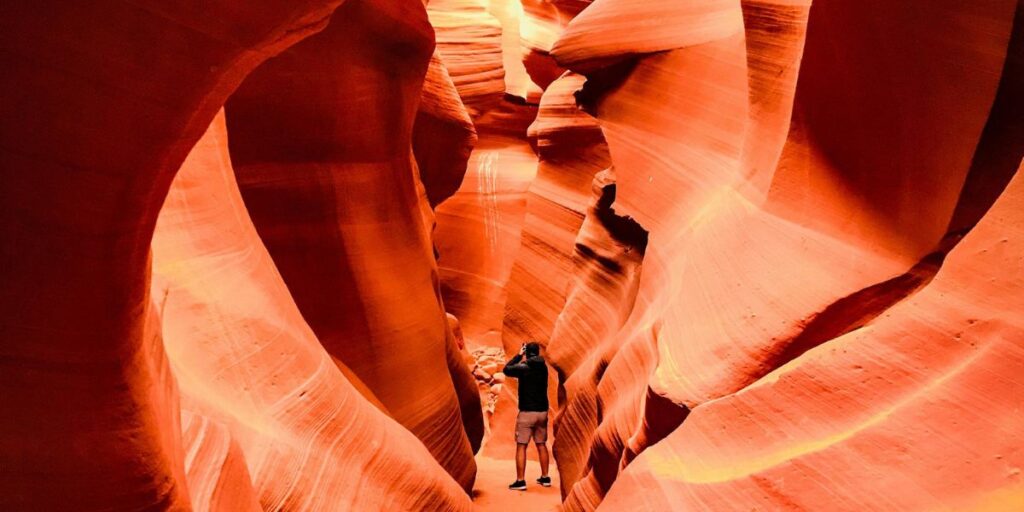 Besucher fotografiert im schmalen Antelope Canyon zwischen hohen, rot-orangen Sandsteinwänden.