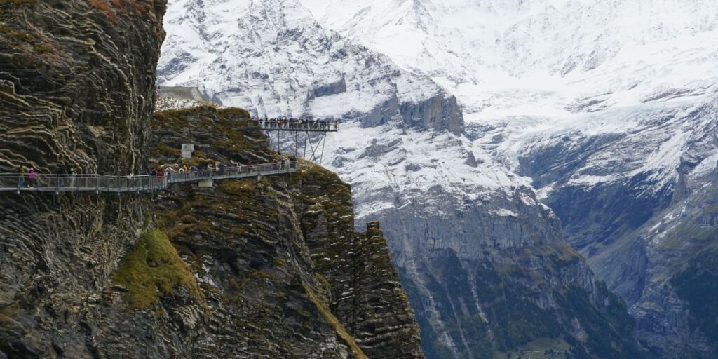 Metallsteg des First Cliff Walk in Grindelwald, entlang einer steilen Felswand mit Blick auf schneebedeckte Berge