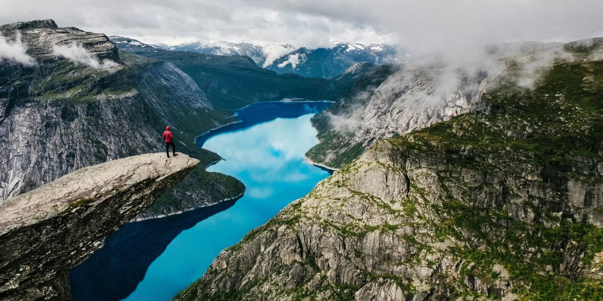 Wanderer steht auf der Trolltunga in Norwegen mit Blick auf den türkisblauen Ringedalsvatnet-See