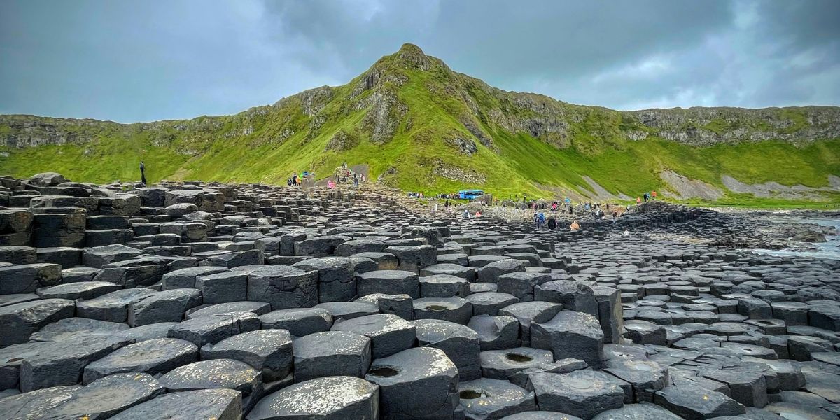 Basaltsäulen des Giant’s Causeway an der Küste Nordirlands mit grünen Hügeln im Hintergrund.