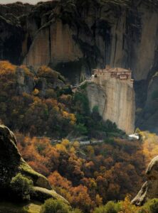 Meteora-Kloster in Griechenland auf einem hohen Felsen, umgeben von buntem Herbstwald und gewaltigen Sandsteinformationen.